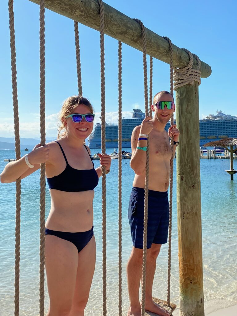 Jake and Emmali standing on swing chairs in front of a cruise ship